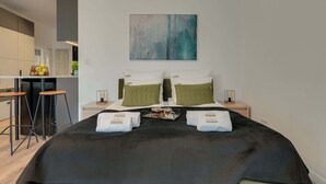 Habitación de hotel con cama, dos mesitas de noche, una zona de bar y un cuadro abstracto grande en la pared.