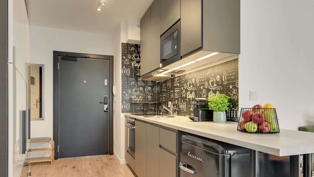 Cocina moderna con electrodomésticos de acero inoxidable, salpicadero negro con diseños de café y un frutero sobre la encimera.