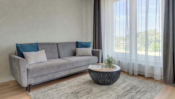 A modern living room with a grey sofa, a round coffee table, and sheer curtains. - Letnicka 31 with Balcony | Perfect Stay (Gdańsk)