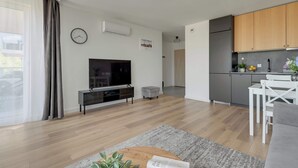 A modern living room with a flat-screen TV, a small sofa, a coffee table, and a dining area with a white table and chairs. - Letnicka 31 with Balcony | Perfect Stay (Gdańsk)