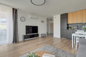 Ein modernes Wohnzimmer mit Flachbildfernseher, einer kleinen Couch, einem Couchtisch und einem Essbereich mit weißem Tisch und Stühlen.