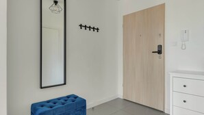 A minimalist room with a large mirror, a wooden door, a white dresser, and a blue bench. - Letnicka 31 with Balcony | Perfect Stay (Gdańsk)