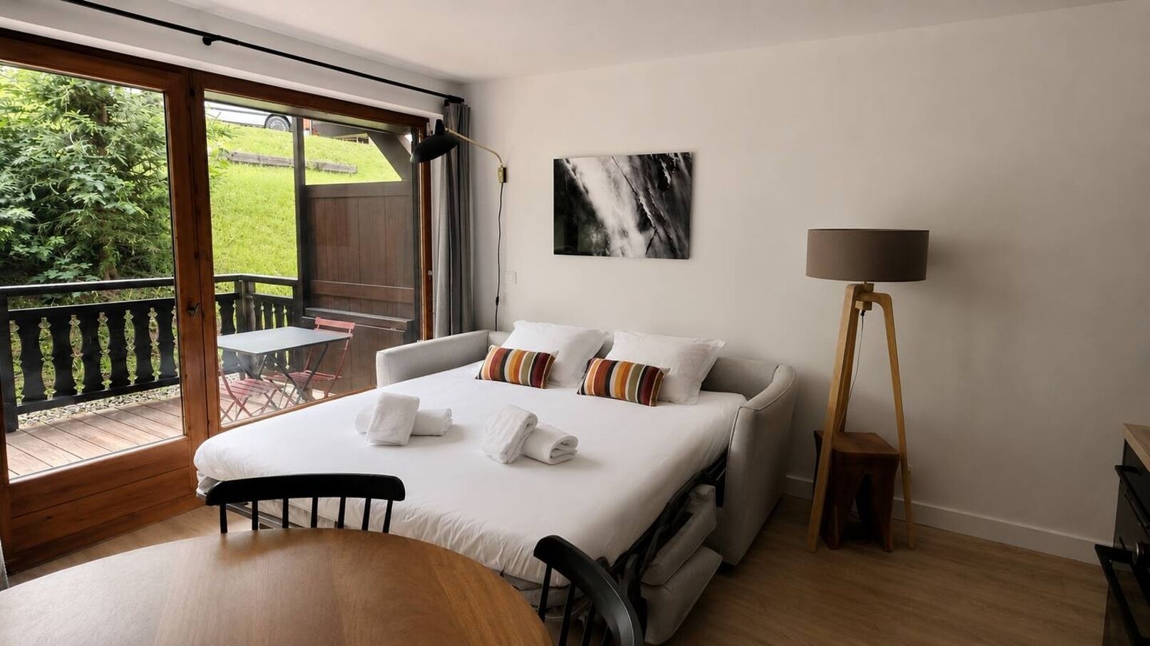 Ein Hotelzimmer mit Bett, Tisch, Stuhl, Sofa, Lampe und Blick ins Freie.