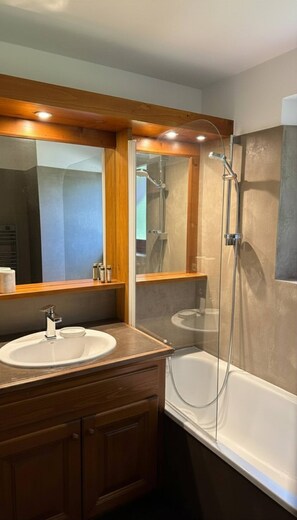 Ein Badezimmer mit einem Holzbadezimmerhocker, einem weißen Waschbecken, einem Spiegel, einer Duschkabine und einer Badewanne.