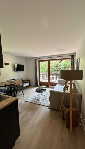 Ein modernes Wohnzimmer mit Essbereich, einem Flachbildfernseher, einem großen Fenster mit Vorhängen und einem Gemälde auf einem Ständer.