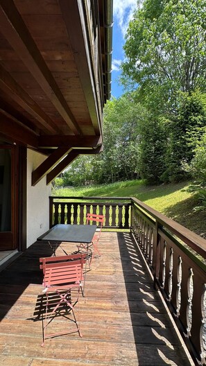 An outdoor patio with a table and chairs, a wooden railing, and a view of a green landscape. - Apartment for 4 people • Balcony • Parking • Close to the slopes (Megève)