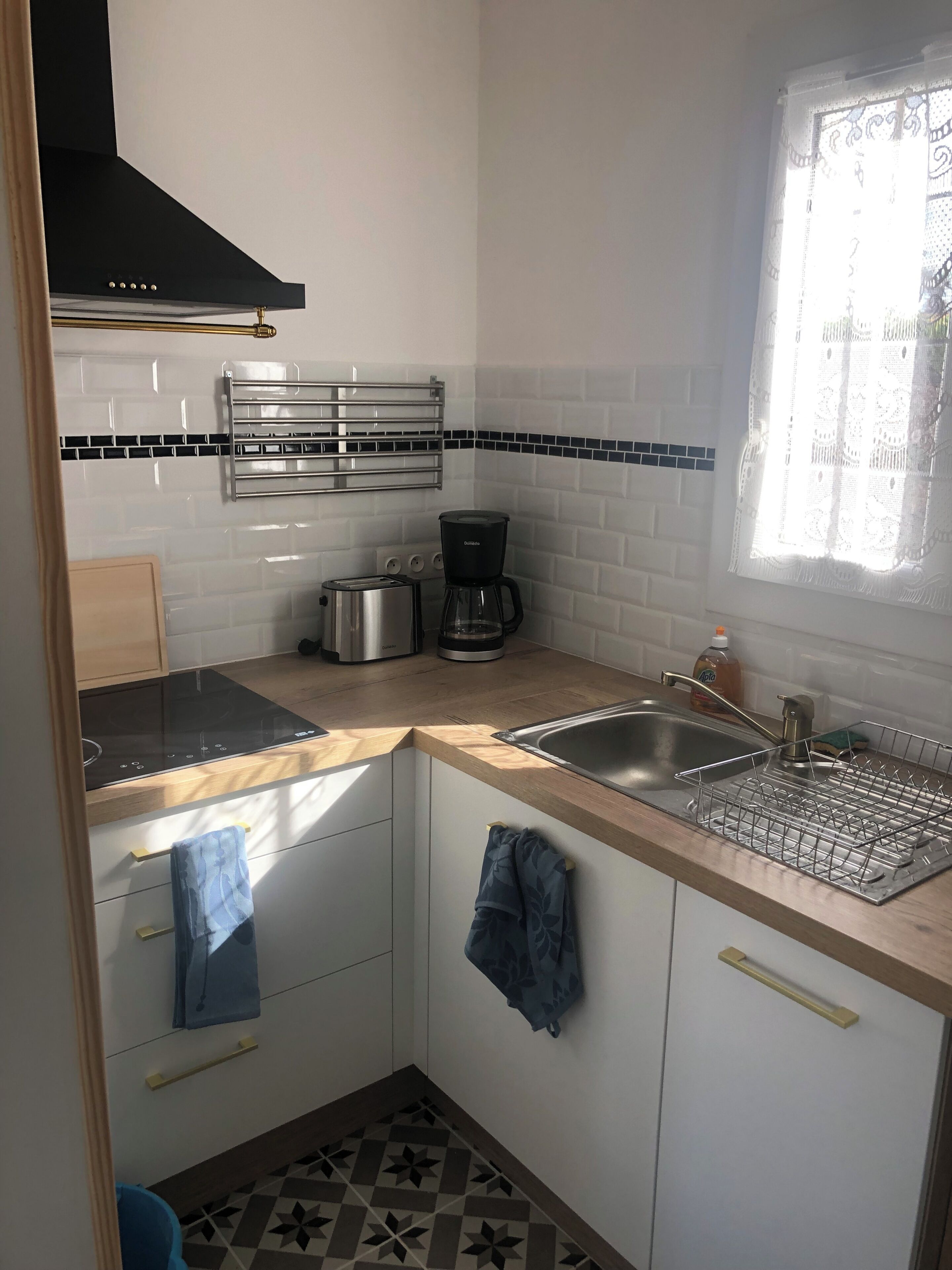 A compact kitchen with a black range hood, a coffee maker, and a stainless steel sink.