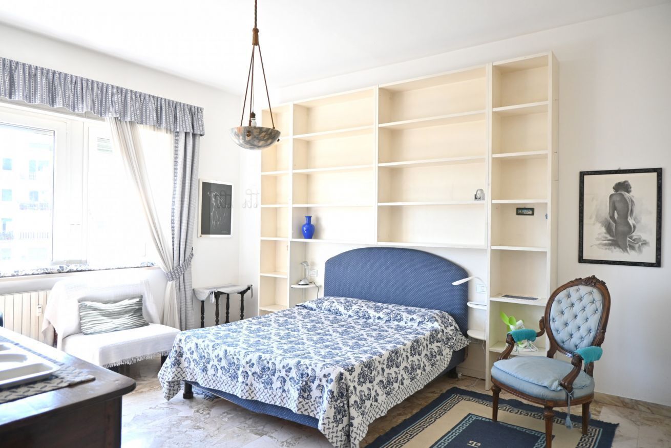 A bedroom with a bed, a chair, a desk, and built-in shelving.