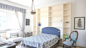 A bedroom with a bed, a chair, a desk, and built-in shelving.