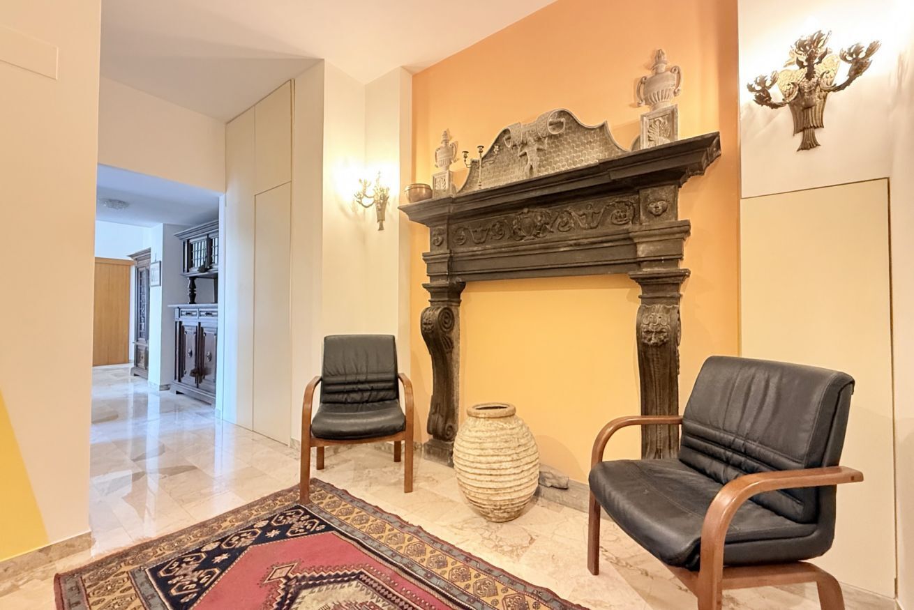 A lobby with a fireplace, two leather chairs, a patterned rug, and a vase.