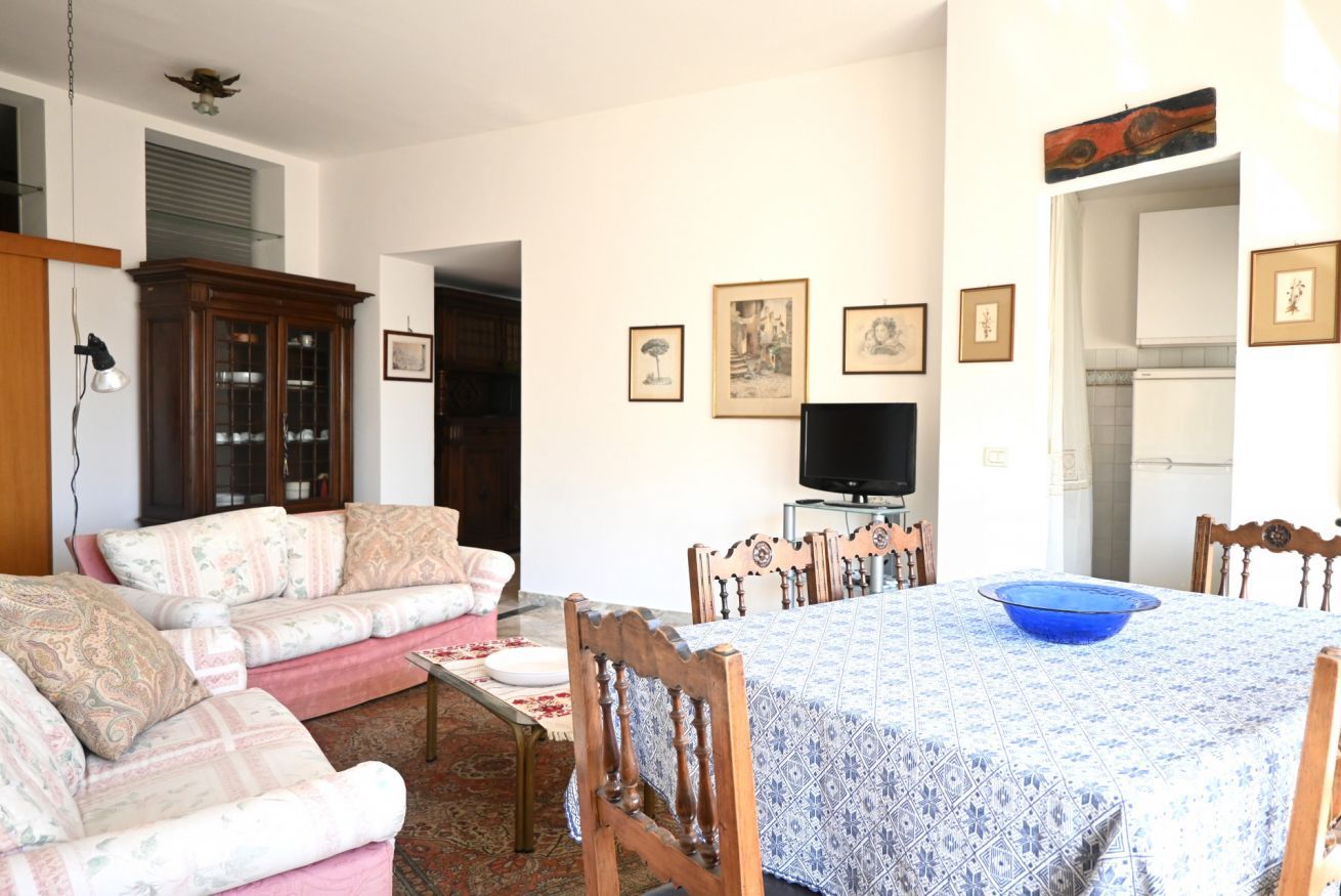 Una sala de estar con sofá, una mesa de comedor con sillas, televisor y cuadros en la pared.