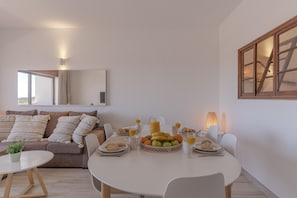 A modern living room with a dining area, a sofa, a coffee table, and a breakfast setup with fruits and pastries. - #386 Comfortable Stay in Montechoro | 2 Bedrooms (Albufeira)