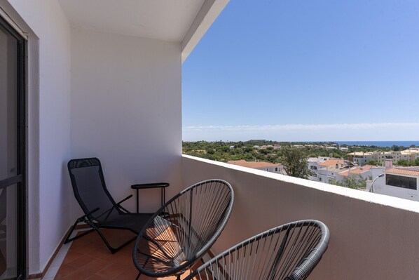 A balcony with two black chairs and a small table, overlooking a coastal town with buildings and greenery. - #386 Comfortable Stay in Montechoro | 2 Bedrooms (Albufeira)