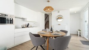 Een moderne keuken met witte kasten, een ingebouwde oven en een eethoek met een ronde tafel en grijze stoelen.