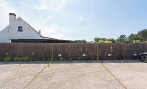 A fenced area with a gravel surface, a building with a white facade and a pitched roof, and a vehicle parked to the side. - Alegria Newport - comfort, nature & coast in 6 min (Koksijde)