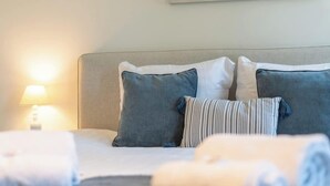 Een keurig opgemaakt bed met kussens, een gestreept kussen, een bedlampje en een schilderij aan de muur.