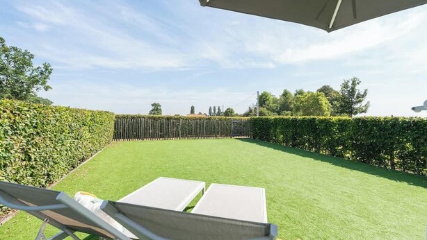 Een verzorgd gazon met een houten omheining, een witte parasol en twee witte stoelen.