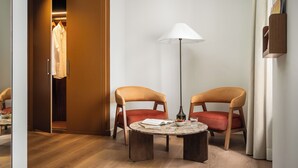 A hotel room with a wooden floor, a round table with chairs, a floor lamp, and a wardrobe with hanging clothes. - Casa Aroa Hotel (Barcelona)