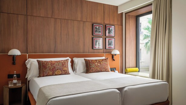 A double bed with two pillows, a nightstand with a lamp, and framed pictures on the wall. - Casa Aroa Hotel (Barcelona)