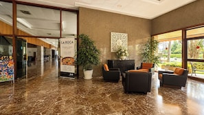 Eine Lobby mit Marmorboden, einer Sitzecke, einem Blumentopf und einem Schild für das Restaurant 'LA ROCA'.