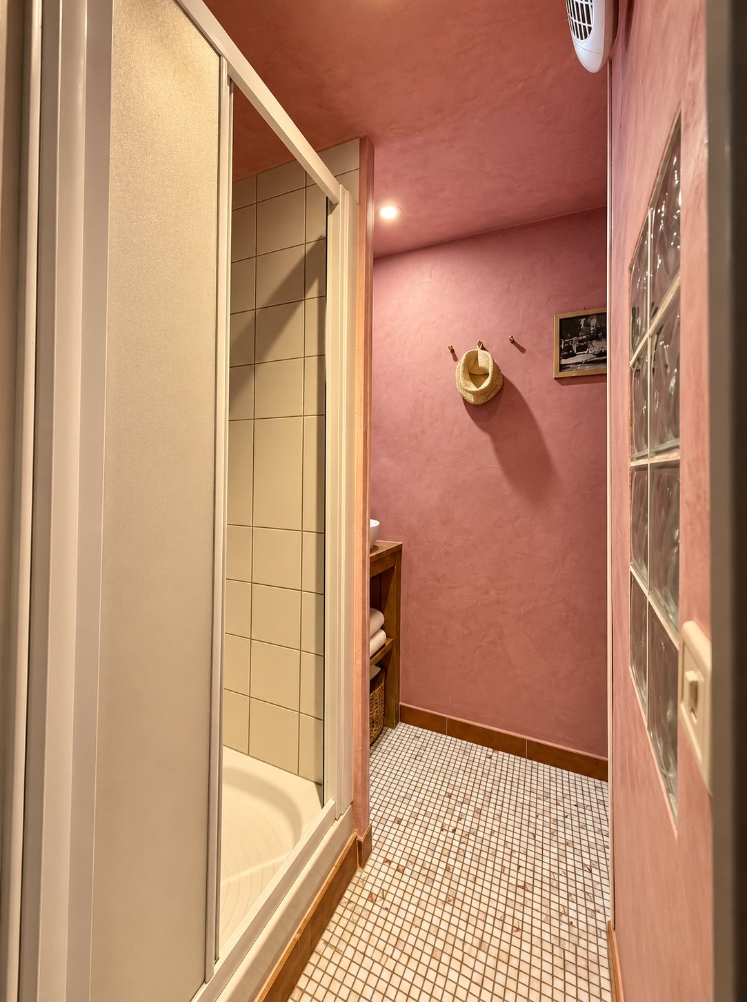 Ein Badezimmer mit Fliesenboden, einer Duschkabine und einer rosafarbenen Wand.