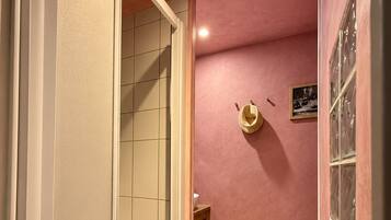 Ein Badezimmer mit Fliesenboden, einer Duschkabine und einer rosafarbenen Wand.
