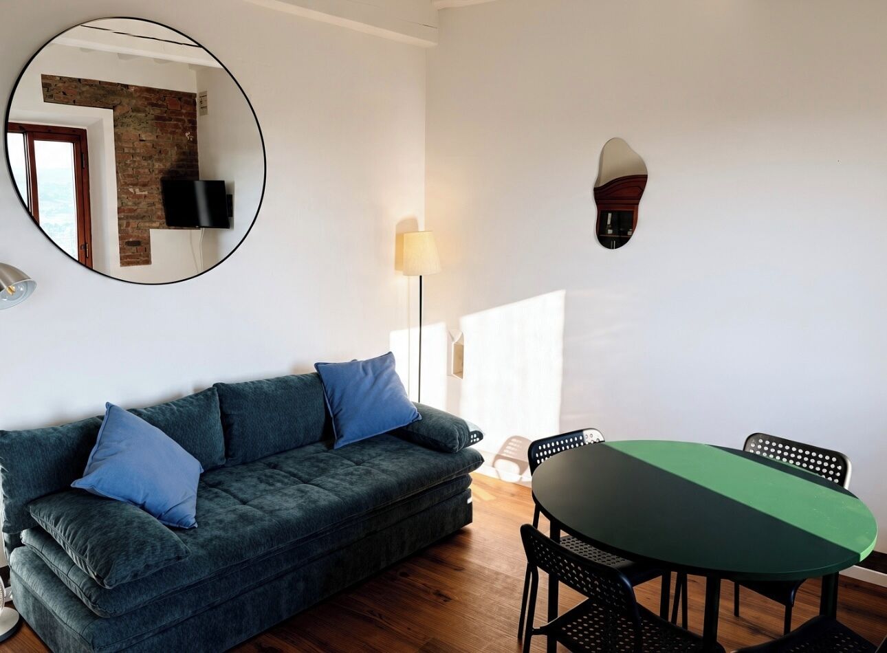 Ein modernes Wohnzimmer mit einem dunkelgrünen Sofa, blauen Kissen, einem runden Tisch und schwarzen Stühlen.