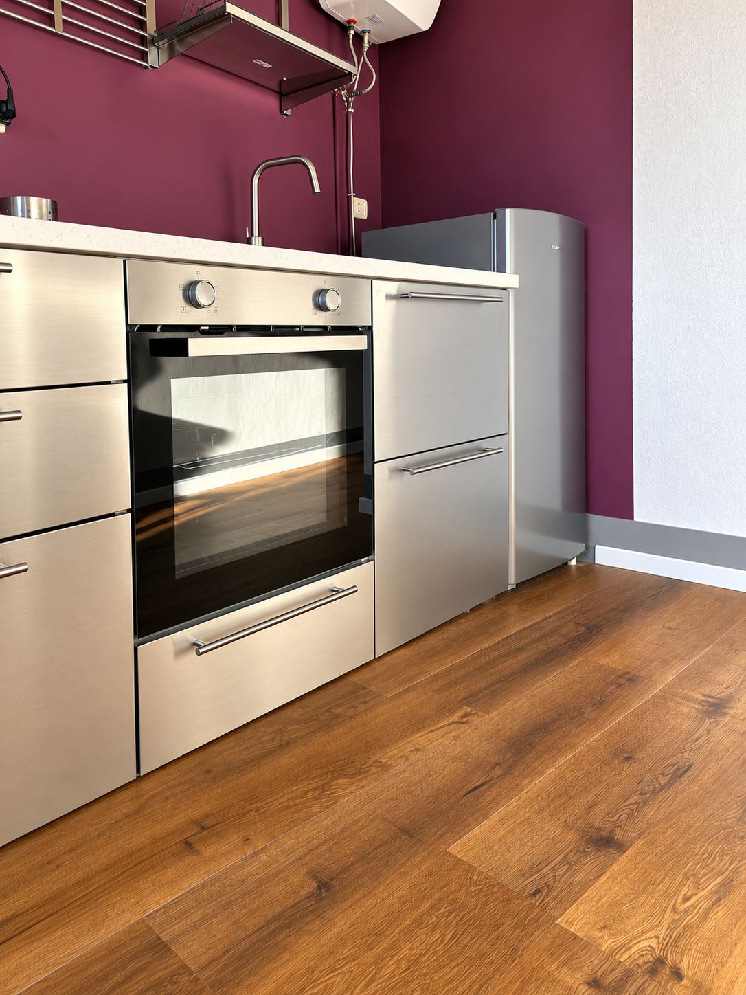 Una cucina moderna con elettrodomestici in acciaio inossidabile, pavimento in legno e una parete d'accento viola.