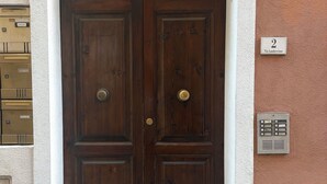 Eine doppelte Holztür mit Messingknauf, eingebettet in einen weißen, gewölbten Rahmen, vor einer strukturierten Wand mit Briefkasten und Hausnummer.