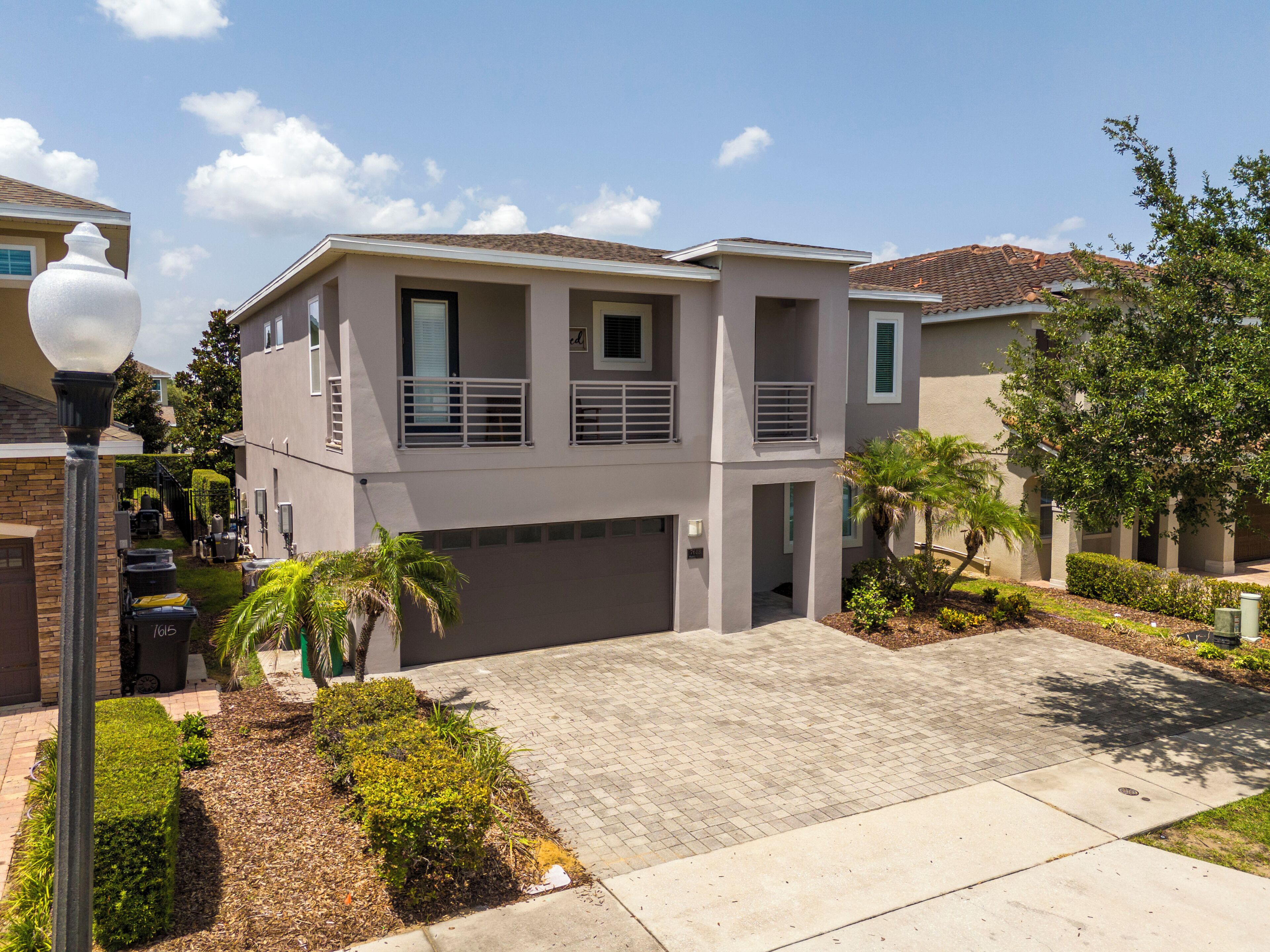 A two-story residential building with a flat roof, a garage, and a landscaped front yard with a palm tree.