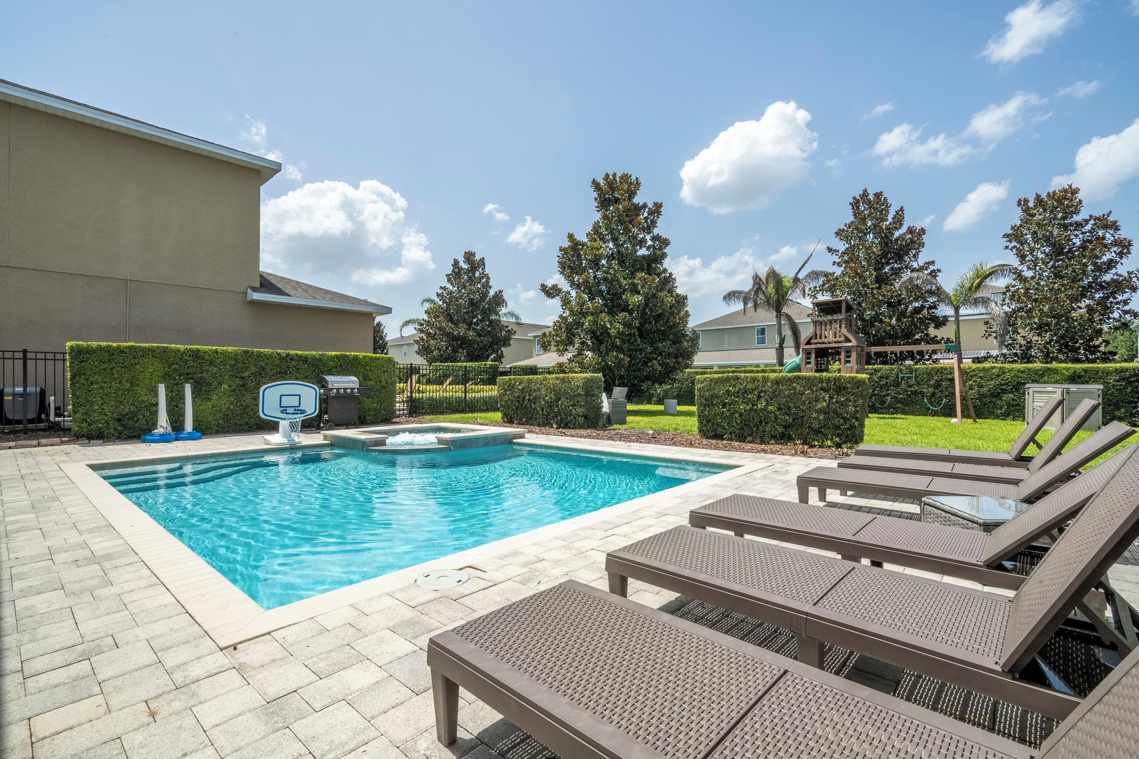 A swimming pool with lounge chairs and a basketball hoop.