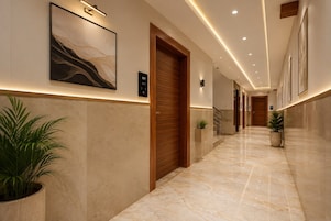 A hotel corridor with marble flooring, wooden doors, and framed artwork on the walls.