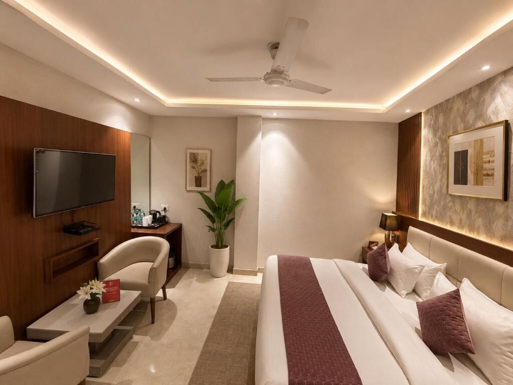 A modern hotel room with a flat-screen TV, a bed with a red blanket, a desk with a chair, a potted plant, and a ceiling fan.