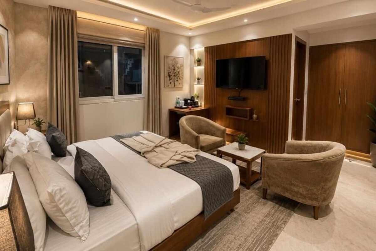 A hotel room with a bed, two chairs, a TV, a desk, and a wardrobe.
