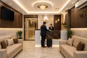 A hotel reception area with a reception desk, two sofas, a television, and a chandelier. - NH Skye Suites Hotel T-3 Delhi Airport  (New Delhi)