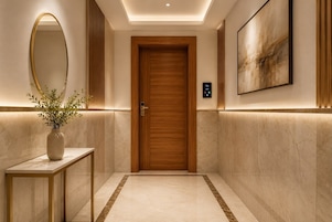 A hallway with a wooden door, a wall-mounted mirror, a vase with plants, and a framed artwork.