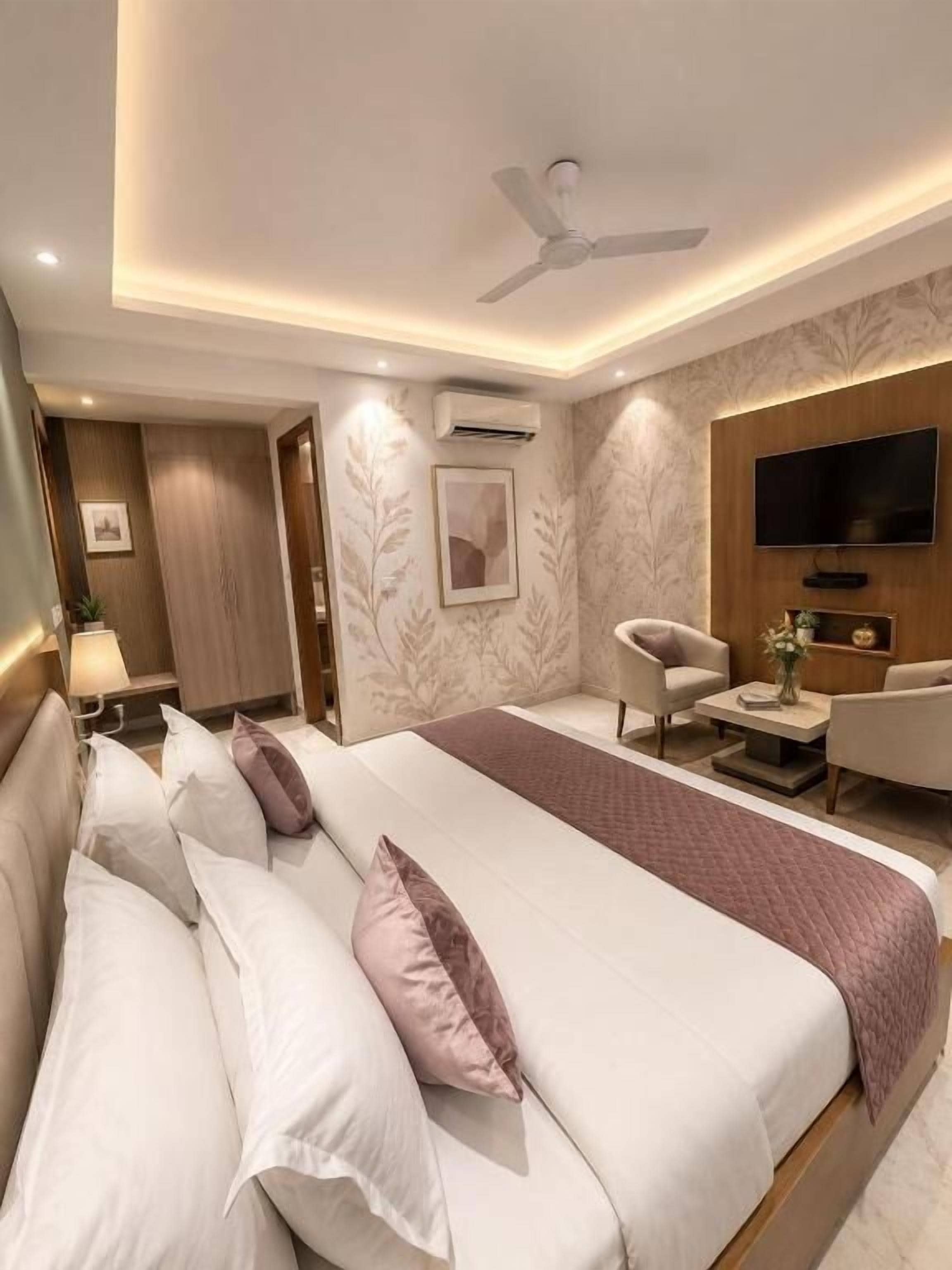 A modern hotel room with a large bed, a flat-screen TV, a seating area, and a ceiling fan.