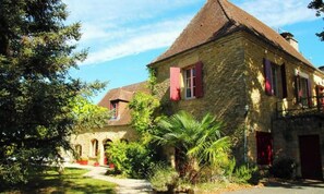 A stone building with a pitched roof, red shutters, and a pathway leading to the entrance. - A stunning historic farmhouse near Sarlat with a private pool set in spacious grounds. (Proissans)