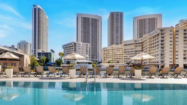 A hotel pool area with lounge chairs and umbrellas, surrounded by high-rise buildings. - Upper Studio Intracoastal & Poolside restaurant (Hallandale Beach)