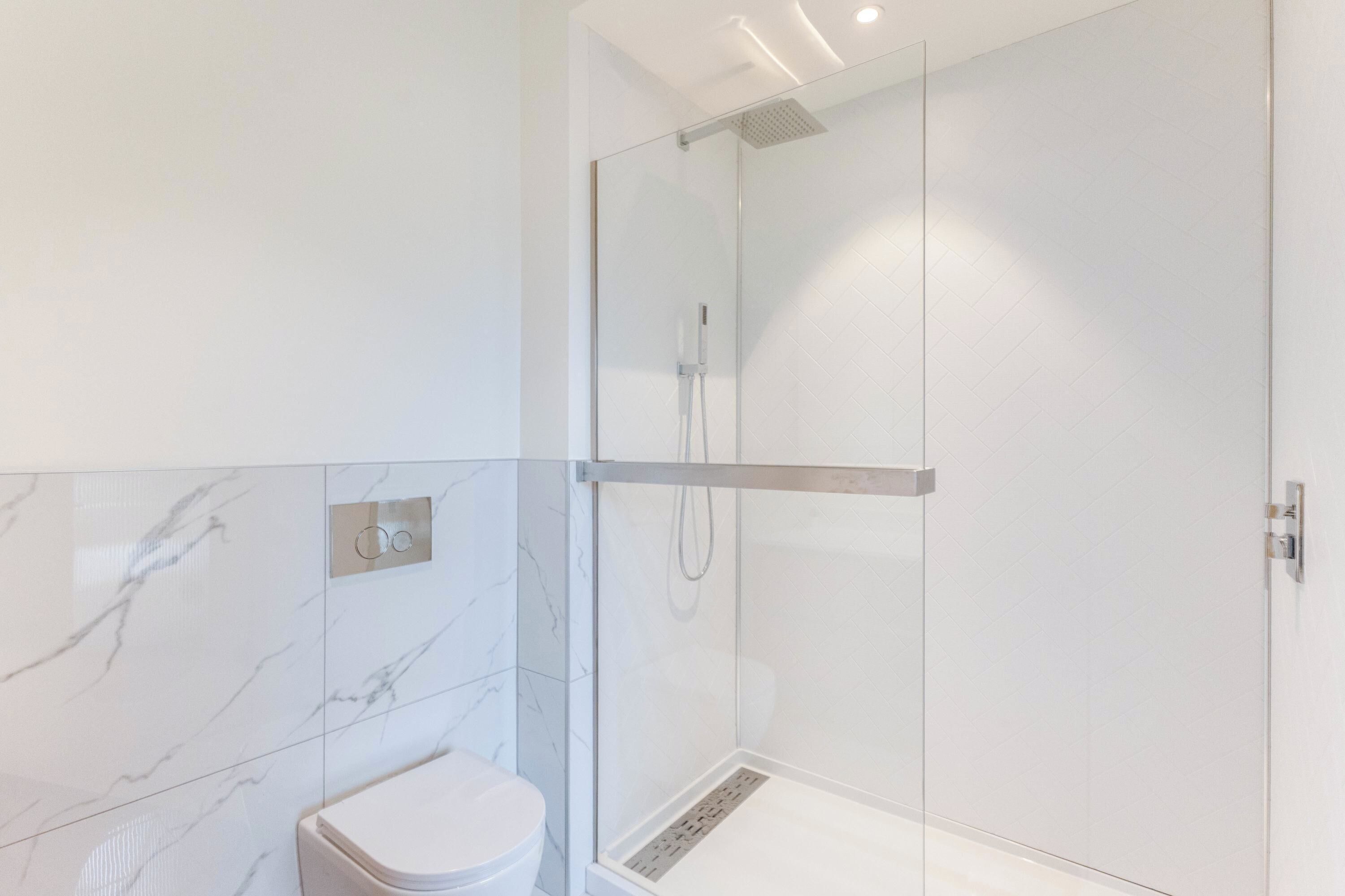 Un baño moderno con ducha envuelta en vidrio, inodoro y paredes con diseño de mármol.