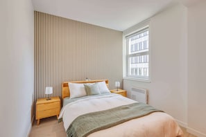 A bedroom with a bed, two bedside tables, a radiator, and a window with blinds. - 313 Cook - Apartment in Old Quebec (Québec)