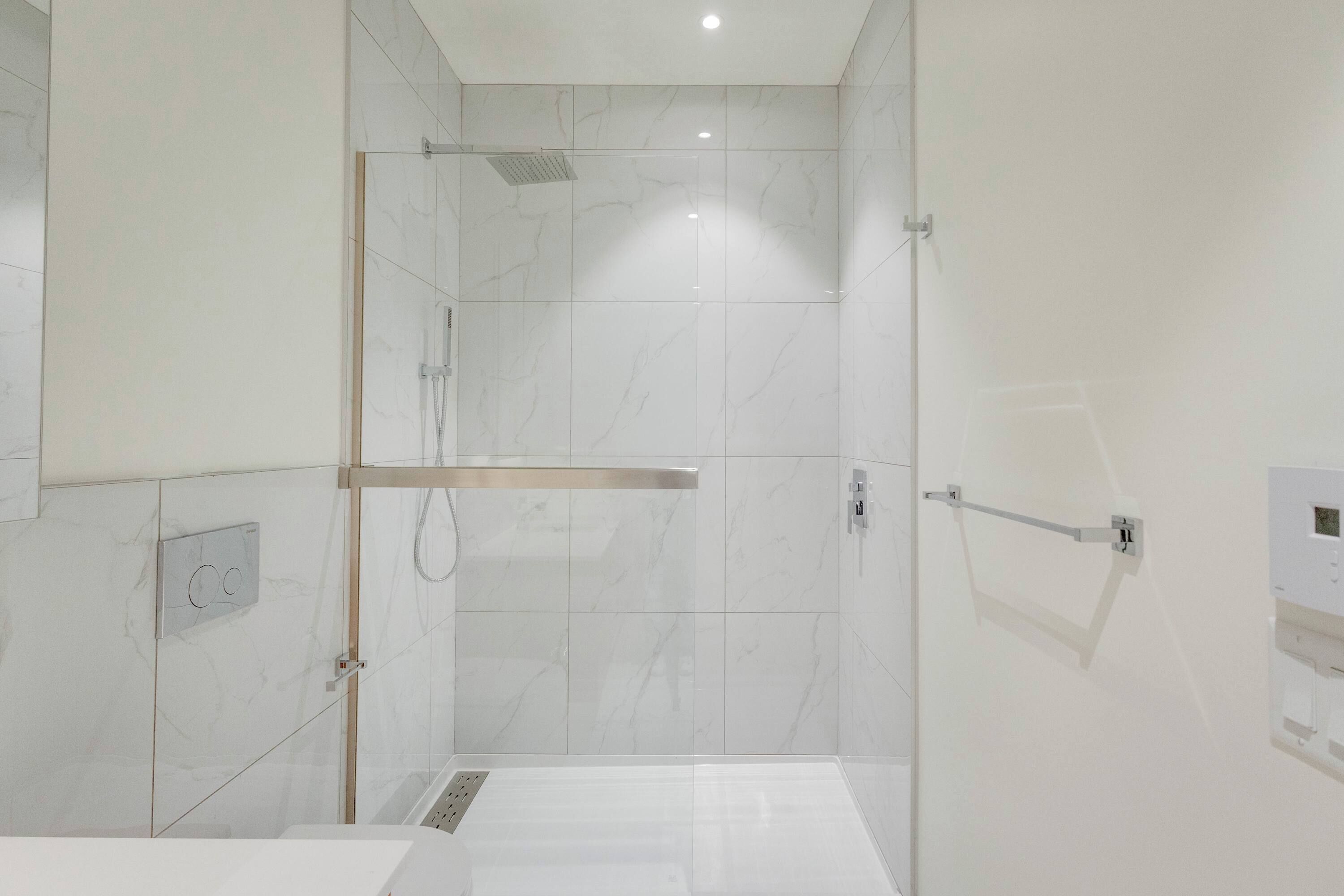 A modern bathroom with a glass-enclosed shower, white marble tiles, and a visible control panel.