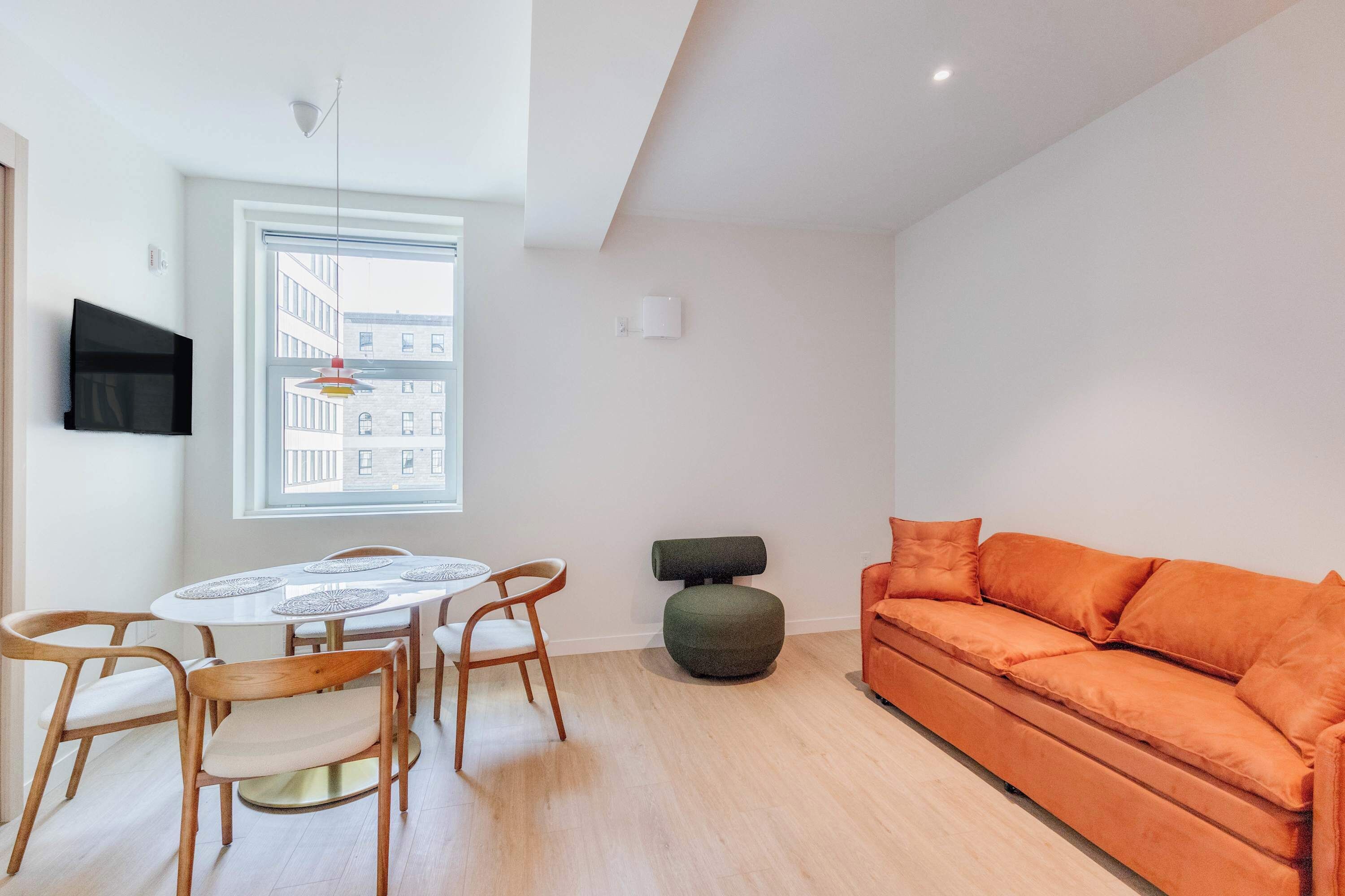 A modern living room with a round dining table, wooden chairs, a sofa, and a television mounted on the wall.