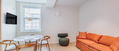 A modern living room with a round dining table, wooden chairs, a sofa, and a television mounted on the wall.