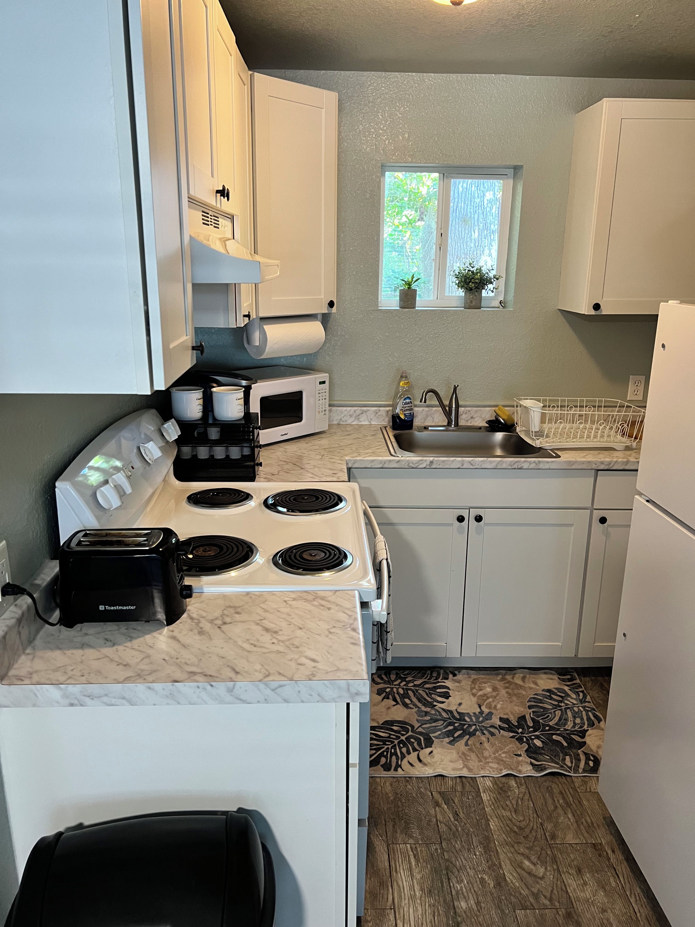A kitchen with white cabinets, a stove, a microwave, a toaster, and a sink.