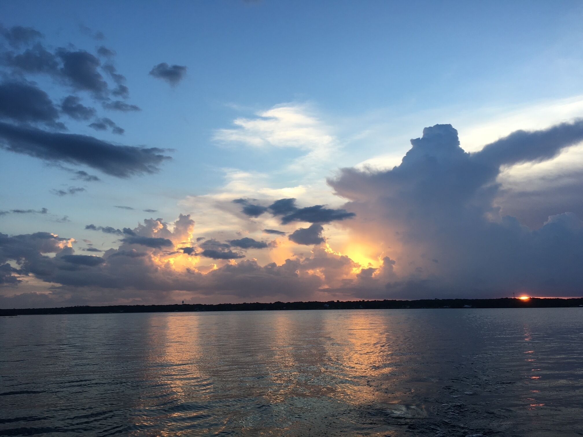 A sunset over a body of water with clouds reflecting on the surface.