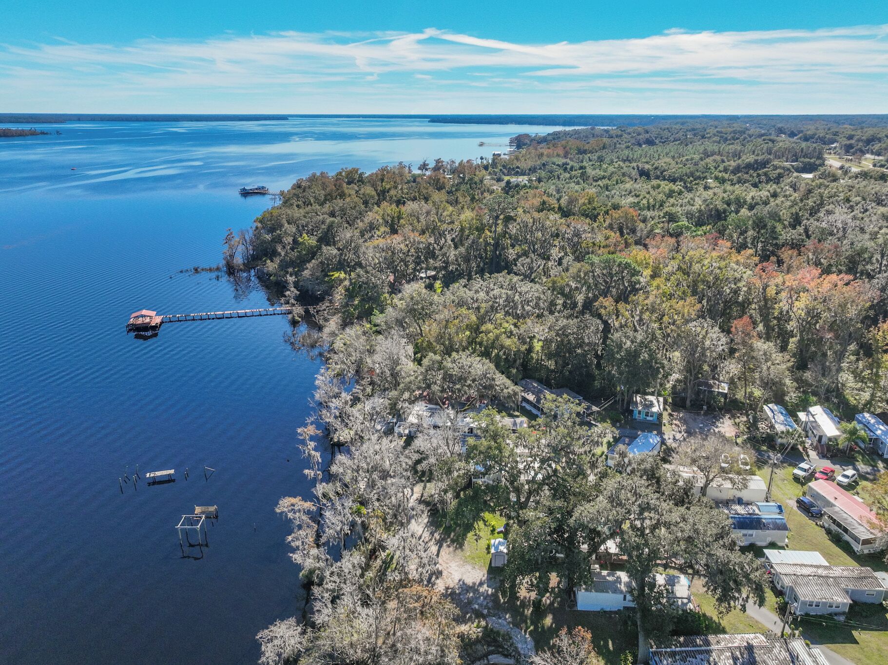 An aerial view of a lakeside property with a dock, boats, and mobile homes.