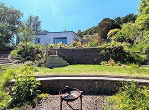 Ein modernes Haus mit einer Steinschmalseite, einer Holztreppe und einem Garten mit verschiedenen Pflanzen.