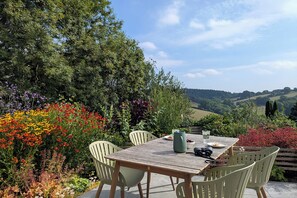 Ein Essbereich im Freien mit Tisch und Stühlen, umgeben von bunten Blumen und Grünpflanzen, mit Blick auf eine reizvolle Landschaft.