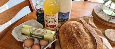 Una mesa con una hogaza de pan, un cartón de huevos, una botella de jugo de manzana, un tarro de café y una botella de leche.